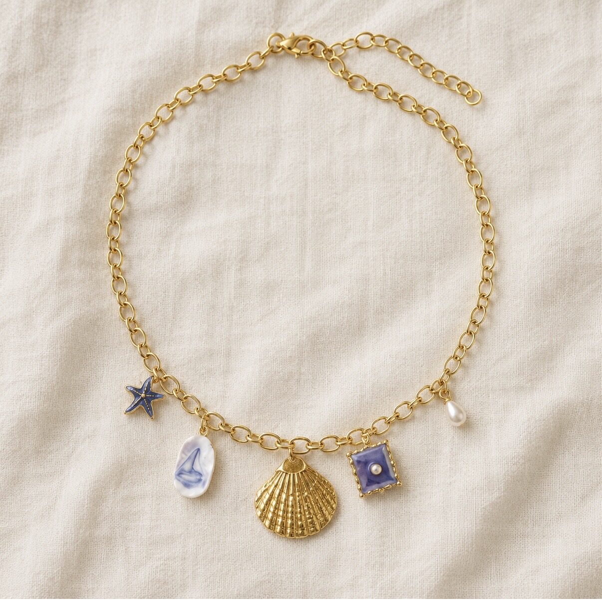 Gold charm necklace with a scallop shell, porcelain sailboat and enamel starfish