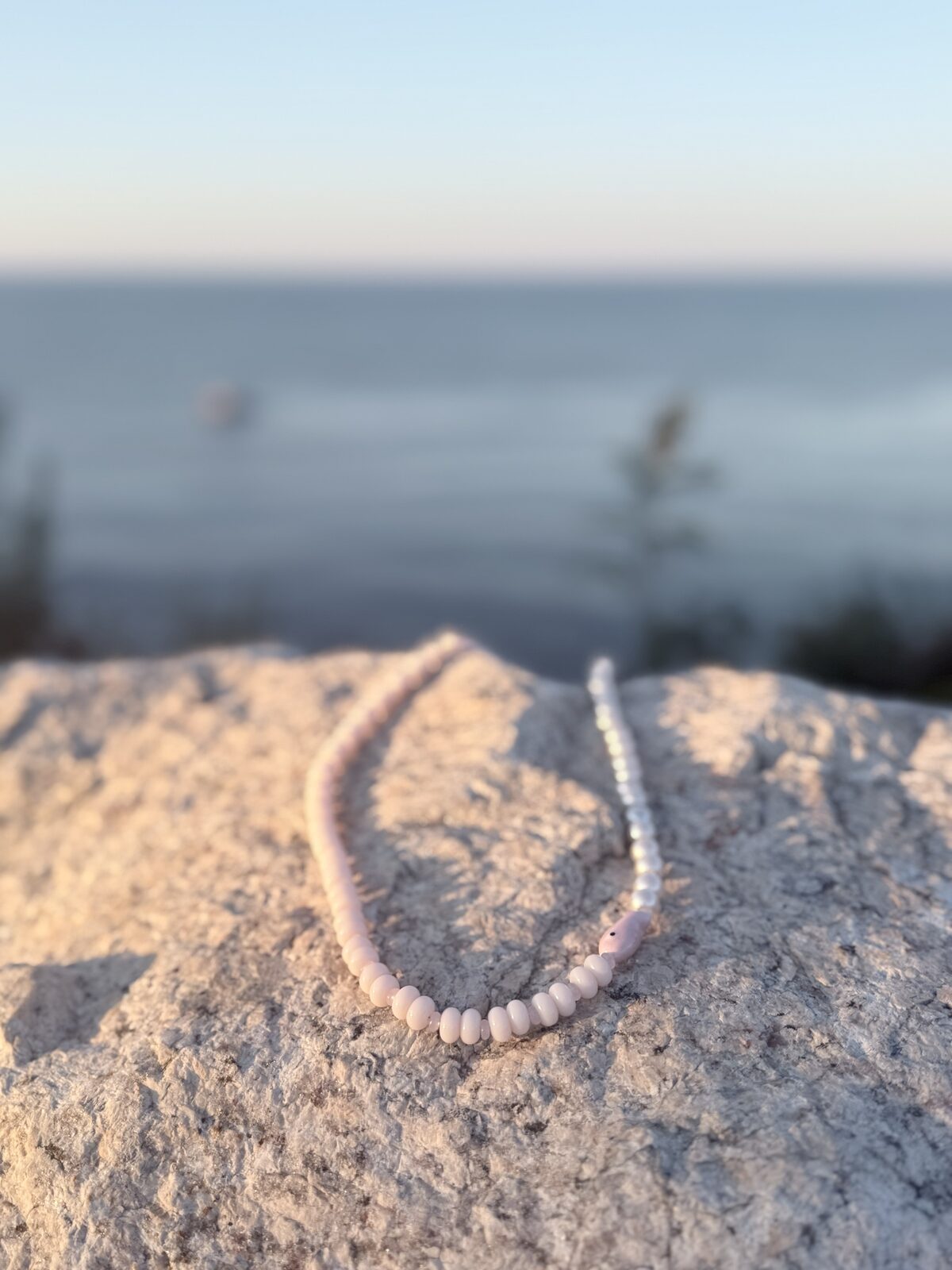 Blush pink beaded necklace on a seaside rock at sunset