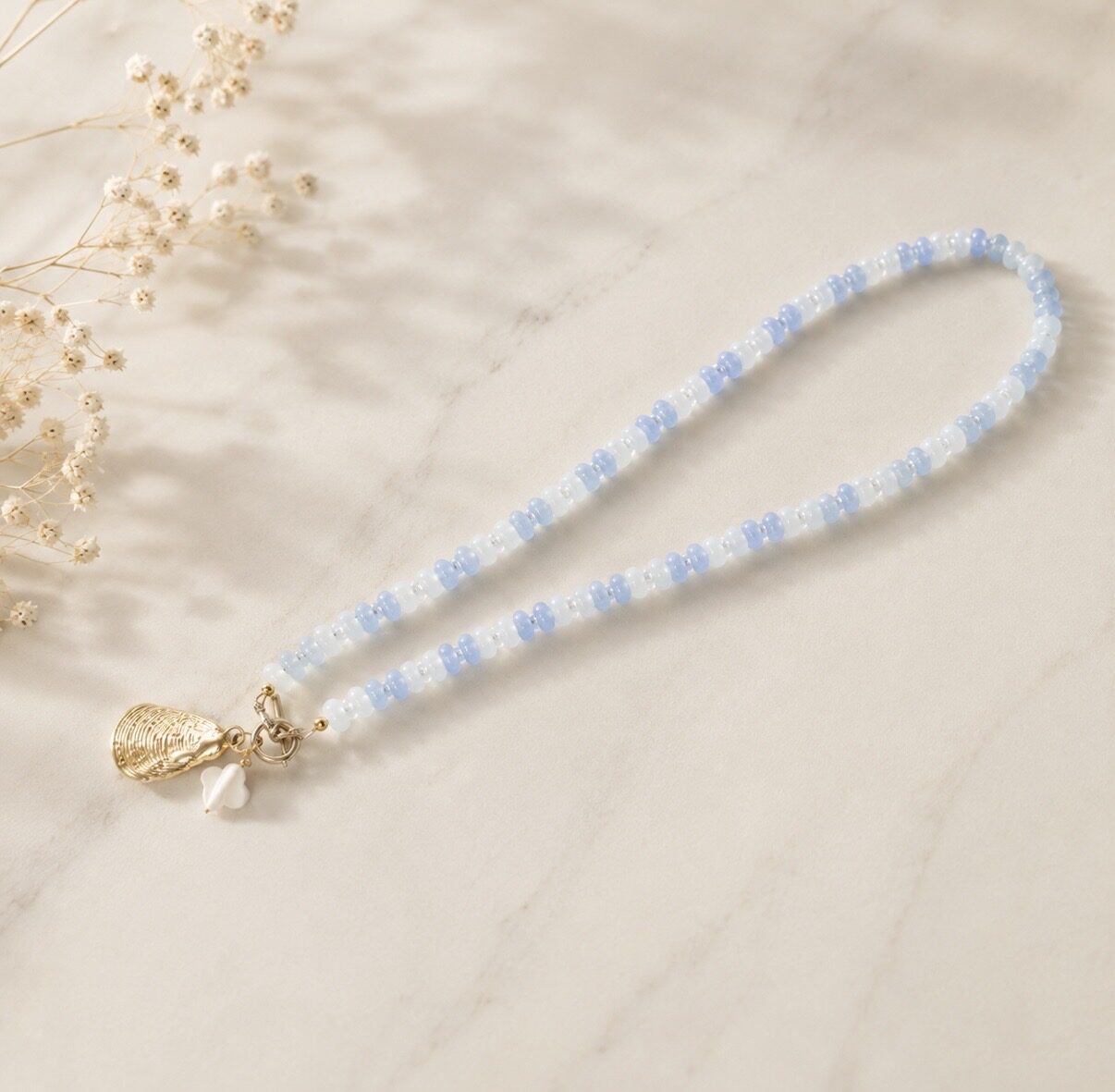 Pale blue and white beaded necklace with a gold oyster charm