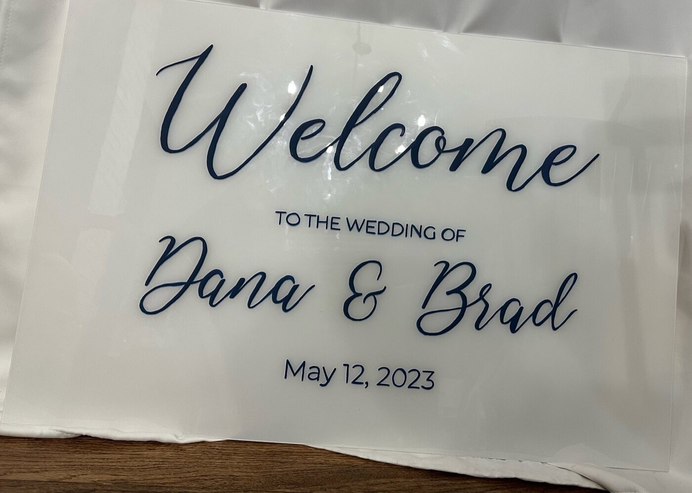 White acrylic wedding welcome sign for Dana and Brad with navy script lettering