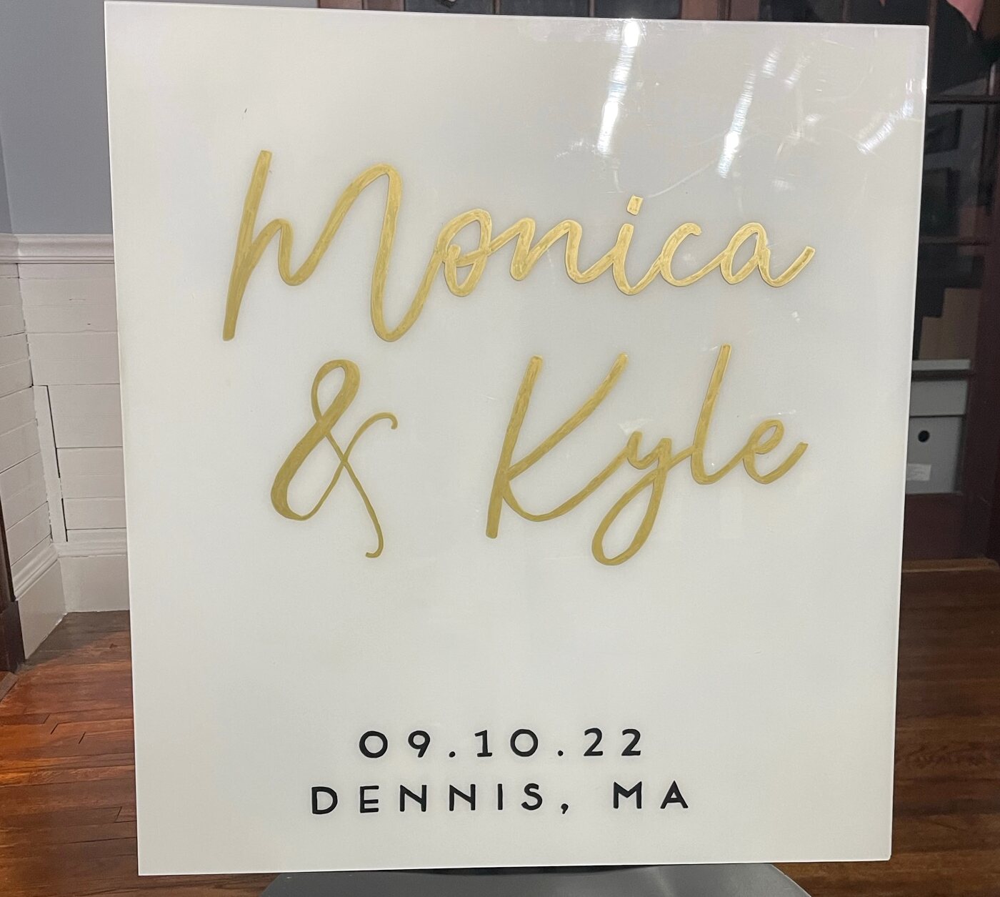 White acrylic sign with raised gold script names Monica and Kyle, dated in Dennis, MA