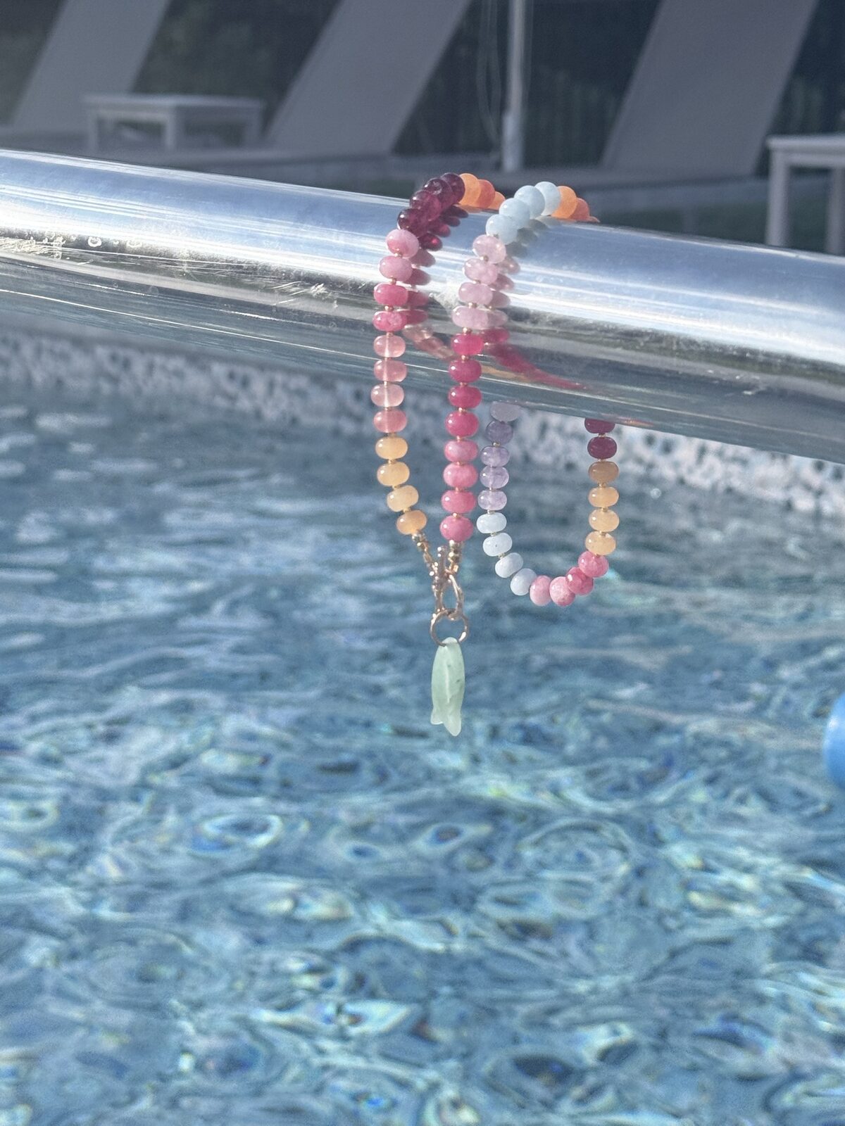 Pink, orange and lavender gemstone necklace with a green fish charm over a pool